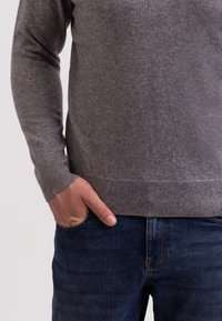 Grau gestrickter Pullover mit langen Ärmeln und gerippten Bündchen, kombiniert mit dunklen Jeans aus Denim mit einer Fronttasche. Weiche Textur, simples Design.