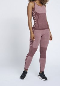 Atletická souprava v barvách mauve, obsahující tílko s texturami na bočním panelu a ladící legíny s chevronovými vzory. Součástí jsou černé tenisky.