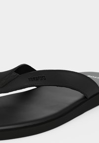 Μαύρη δερμάτινη σαγιονάρα με ανάγλυφο λογότυπο BOSS στο λουράκι και λεία σόλα, εμφανιζόμενη σε απλό λευκό φόντο.