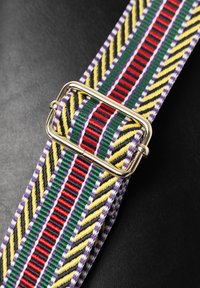 Cinghia tessuta colorata con strisce diagonali in verde, giallo, rosso, nero e viola, con un dettaglio di fibbia rettangolare dorata.