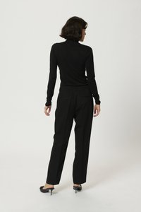 Haut noir à col roulé associé à un pantalon noir ajusté. Modèle de dos, mettant en valeur une silhouette épurée et des mules à talons à bout pointu.