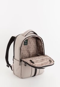 Mochila gris con un material exterior suave, con un interior de patrón hexagonal, bolsillo frontal y cremalleras negras. Dos correas de hombro acolchadas.