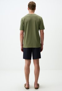 Oliwkowy t-shirt z krótkim rękawem w połączeniu z granatowymi szortami. Miękka tekstura, luźny krój, prosty design. Sandały z prostym detalem w postaci paska.