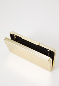 Gullfarget metallisk clutch-lommebok med en slank rektangulær form, med en teksturert ytre, svart innside og en sikker klaffelås.