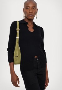 Μαύρος ριγωτός πουλόβερ με γιακά και λαιμόκοψη σε σχήμα κλειδώματος, σε συνδυασμό με μια πράσινη σουέτ τσάντα με αντίθετο λουρί και μεταλλικά αξεσουάρ.