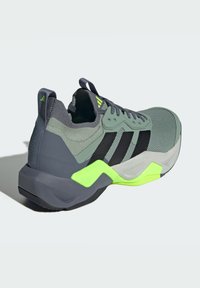 Baskets de sport grises et vertes avec tige en maille, rayures noires et semelle texturée. Présente un talon proéminent et des accents jaunes fluo.