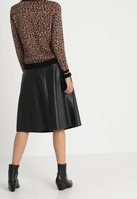 Brun leopardmönstrad tröja med svart ribbad kant, parat med en svart plisserad läderkjol och svarta ankelstövlar.