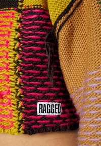 Gebreide trui met een patchworkontwerp in levendige kleuren: roze, geel, zwart en bruin. Inclusief een wit label met "RAGGED."