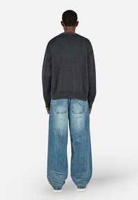 Melnā adīto džemperis ar brīvu piegriezumu un ribotām malām, apvienots ar gaiši ziliem plašiem džinsu biksēm ar aizmugurējām kabatām un izbalējušu tekstūru.