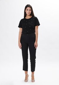 Maglietta nera a maniche corte con borchie argento, abbinata a pantaloni neri su misura e sandali con tacco alto argento scintillanti.