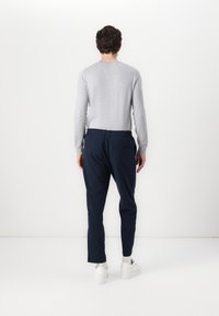 Grauener langärmeliger Pullover und marineblaue, taillierte Hose mit elastischem Bund. Das Outfit wird mit weißen Sneakers abgerundet. Minimalistisches Design.