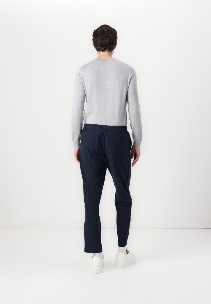 Pull gris à manches longues et pantalon tapered navy avec une taille élastique. La tenue est complétée par des baskets blanches. Design minimaliste.