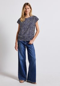 Top blu navy a motivi con maniche corte, abbinato a jeans in denim a gamba larga con una tonalità media, caratterizzati da un fit rilassato e una sottile texture.