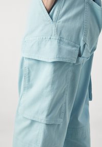 Lichtblauwe cargo pants hebben meerdere zakken, een relaxte pasvorm en een zachte stof met zichtbare stiksels en een gladde structuur.