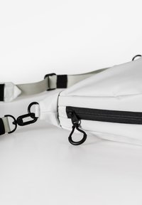 Weiße Umhängetasche aus glattem Material, ausgestattet mit einem schwarzen Reißverschluss, verstellbarem Gurt und Metallbeschlägen mit einem charakteristischen Hakenverschluss.