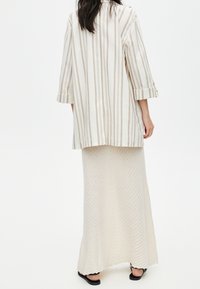 Striped beige and cream oversized shirt with rolled sleeves, paired with a textured cream maxi skirt featuring a zigzag pattern.
