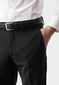 Schwarze Anzughose mit flachem Vorderteil, glatter Textur und schrägen Taschen. Ein schwarzer Ledergürtel mit einer silbernen Metallschnalle ist sichtbar.