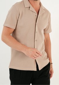 Beige kortärmad skjorta med en strukturerad, ribbad tyg. Klassisk krage och knäppning fram. Anpassad passform, tillsammans med svarta byxor.