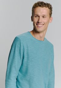 Lichtblauw lange mouwen shirt van een gestructureerde stof met een ronde halslijn en zichtbare stiksels op de mouwen en het lichaam.