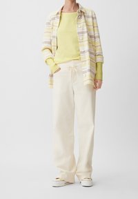 Randig skjorta i mjuk gul, beige och vit; kombinerad med en ljusgul topp och cremefärgade vida byxor. Skorna är vita plattformssneakers.