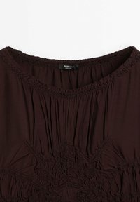 Encolure de blouse marron foncé avec tissu froncé et détails de broderie texturée, montrant une petite étiquette noire portant l'inscription "Massimo Dutti Made in India."