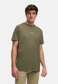 Camiseta de algodón verde oliva con mangas cortas, cuello redondo y un logo blanco en el pecho. Textura suave, corte casual.