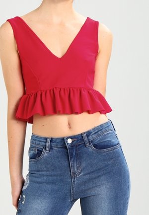 Žena v červeném bezrukávovém crop topu s volánkovým okrajem a v modrých vysoce střižených džínách s lehkým opotřebením.