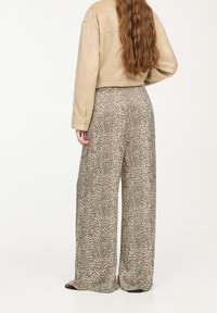 Pantalon à jambes larges en tissu imprimé animal beige et marron, avec une coupe ample et une texture douce, accompagné d'une veste assortie beige clair.