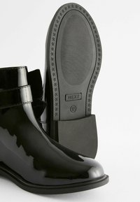 Schwarze, glänzende Stiefeletten mit glatter Oberfläche, abgerundeter Zehenpartie, elastischen Seitenpaneelen und einer gummierten Sohle mit strukturiertem Grip.