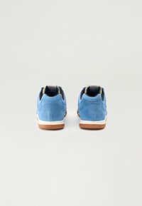 Sneakers din suede albastru cu o talpă intermediară albă și o talpă exterioară din cauciuc maroniu. Prezintă un interior negru și o etichetă mică pe călcâi pentru etichetare.