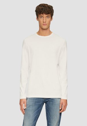 Langärmliges weißes T-Shirt aus weichem Stoff, mit Rundhalsausschnitt und einem dezenten Logo auf der Brust, kombiniert mit blauen Jeans.