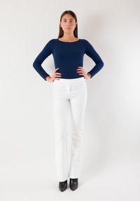 Top a maniche lunghe color blu navy abbinato a pantaloni bianchi aderenti e stivali neri con tacco. Design semplice, texture liscia e vestibilità sagomata.