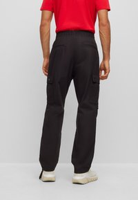 Black cargo pants with an elastic waistband, side pockets, and a relaxed fit, paired with light-colored sneakers on a neutral background.