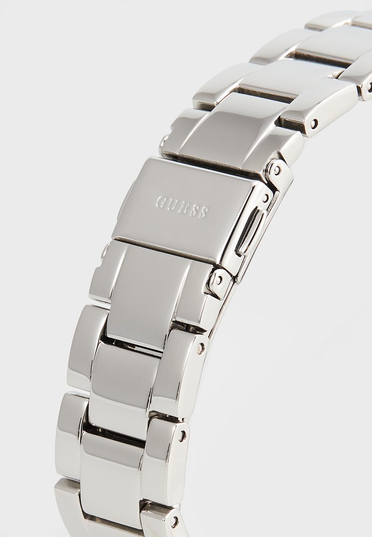 Bracciale per orologio in acciaio inox argentato con maglie rettangolari, dotato di una finitura spazzolata e di una chiusura incisa con il nome del marchio "GUESS."