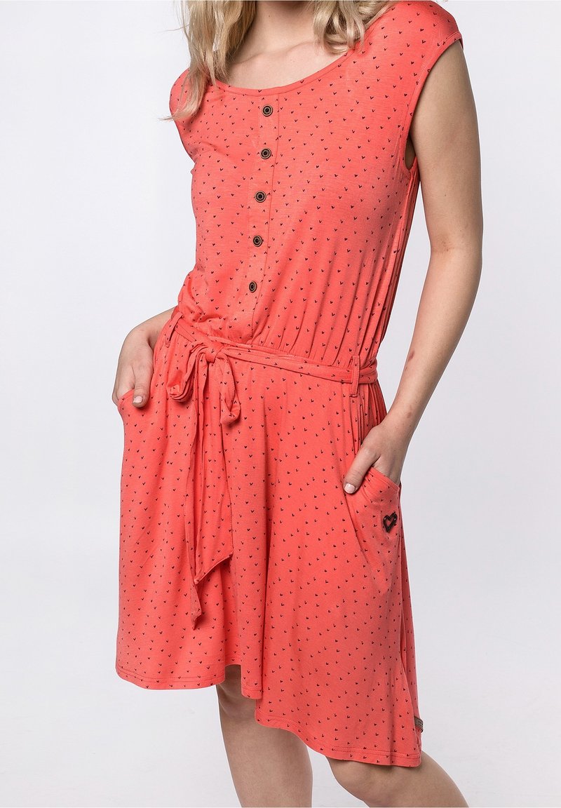 Korálové šaty vyrobené z měkké tkaniny, s krátkými rukávy, kulatým výstřihem, zapínáním na knoflíky a černými vzory srdcí. Mají uvázaný pás a postranní kapsy.