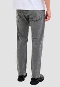 Szare jeansy z denimu o prostym kroju nogawki, z pięcioma kieszeniami i widocznymi detalami przeszyć, zestawione z czarnym obuwiem.