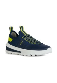 Zapatillas deportivas azul marino con suela blanca, parte superior de malla texturizada, acentos amarillos y cordones elásticos; cinta en el talón para ponerlas y quitarlas fácilmente.