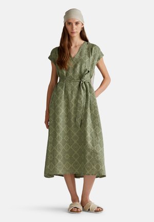 Robe midi à motifs verts avec des manches courtes, un design enroulé et une taille nouée. Dotée d'un motif losange et de poches latérales, associée à des sandales beiges.