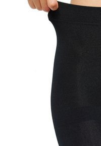 Leggings negros con textura acanalada y un acabado suave. La cinturilla está siendo estirada, mostrando flexibilidad y elasticidad. Diseñados para comodidad y ajuste.