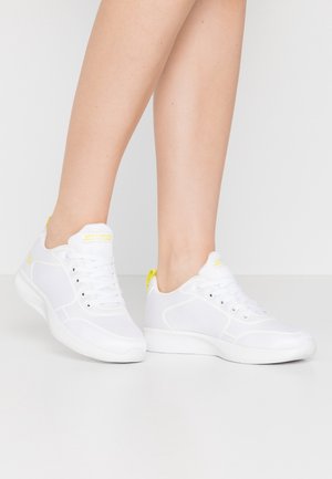 Baskets blanches faites de mesh et de matériaux synthétiques ; dotées de lacets, d'un col rembourré et de accents jaunes vifs sur la languette et le talon.