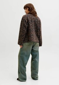 Brun og svart leopardmønstret fleecejakke med løs passform, kombinert med løse blågrønne jeans. Synlig tekstur i stoffet.