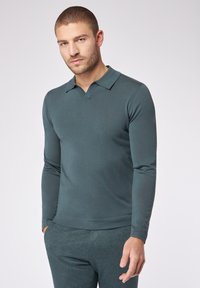 Langarm-Polohemd in dunkeltürkis, aus geripptem Stoff. Hat einen V-förmigen Kragen und eine schmale Passform, kombiniert mit passenden Hosen.