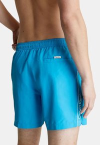 Costumi da bagno blu realizzati in materiale leggero, dotati di un elastico in vita, tasca laterale e un logo bianco lungo la cucitura laterale.