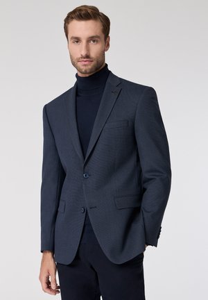 Dark blue blazer with a subtle textured pattern, single-breasted buttons, and notch lapels worn over a fitted turtleneck sweater.