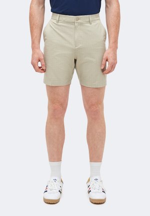 Beige karierte Shorts, getragen mit weißen Sportsocken und weißen Turnschuhen mit blauen und roten Streifen.