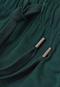 Donkergroene sweatpants met een gestructureerde stof, een elastische trekkoordtaille en metalen aglets op de trekkoorden.