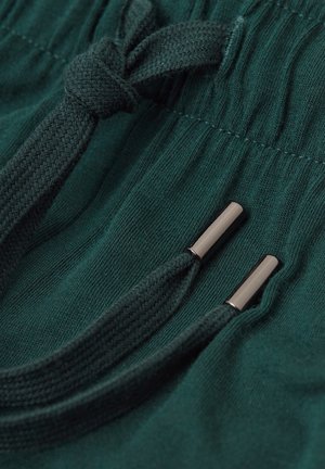 Tmavě zelené tepláky s texturovanou tkaninou, elastickým stahováním v pase a metalickými konci na stahovacích šňůrkách.