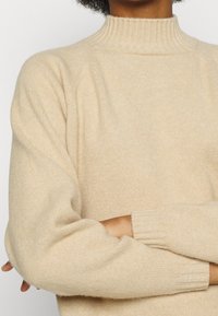 Maglione beige in maglia con colletto alto a coste, maniche raglan e polsini a coste. Texture morbida con una vestibilità rilassata.