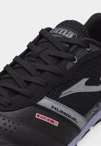 Μαύρο αθλητικό παπούτσι με πλέγμα στην επάνω πλευρά, μαύρα κορδόνια, γκρι λεπτομέρειες και το λογότυπο "Mundial" στο πλάι κοντά σε κόκκινη και λευκή ετικέτα "Piel".