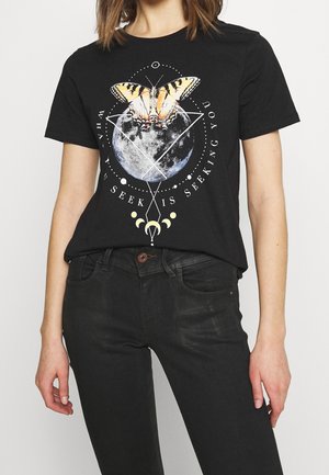 Černé tričko se žlutým a černým motýlem na pozadí úplňku, geometrické tvary a text "To, co hledáš, hledá i tebe."